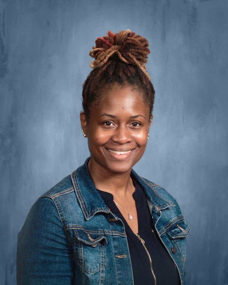 Picture of black woman with locs in a high pony tail wearing a blue jean jacket and blue backdrop